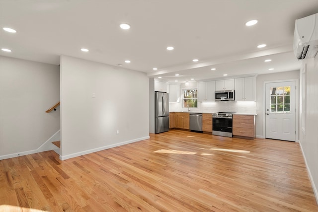 kitchen with appliances with stainless steel finishes, backsplash, an AC wall unit, light hardwood / wood-style floors, and white cabinetry