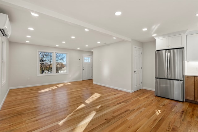 interior space featuring stainless steel fridge, light wood-type flooring, white cabinetry, and a wall unit AC