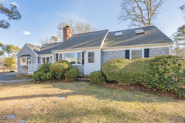 view of front facade with roof with shingles, a chimney, and a front yard