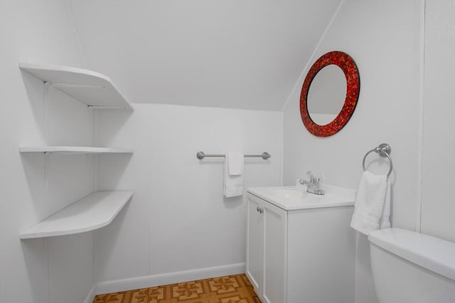 bathroom with lofted ceiling, vanity, toilet, and baseboards