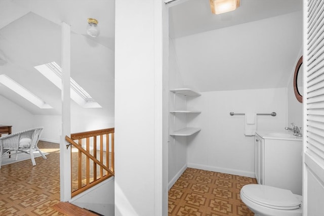 bathroom with toilet, vaulted ceiling with skylight, vanity, and tile patterned floors