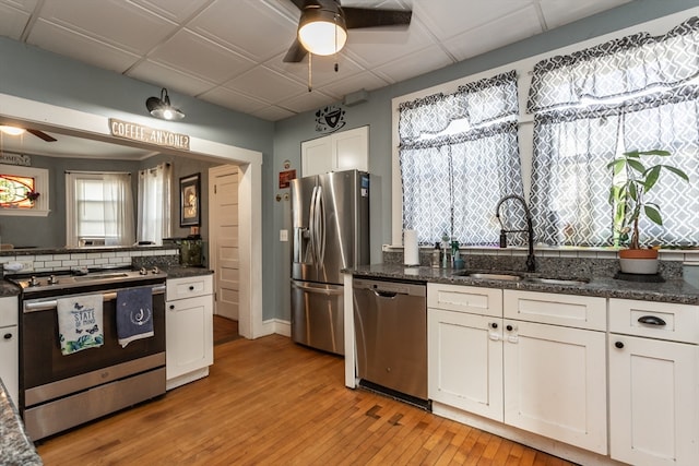 kitchen with white cabinetry, stainless steel appliances, sink, ceiling fan, and light hardwood / wood-style floors