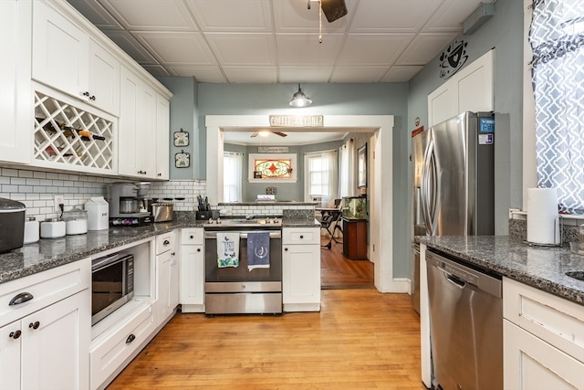 kitchen with dark stone countertops, white cabinetry, light hardwood / wood-style flooring, ceiling fan, and appliances with stainless steel finishes