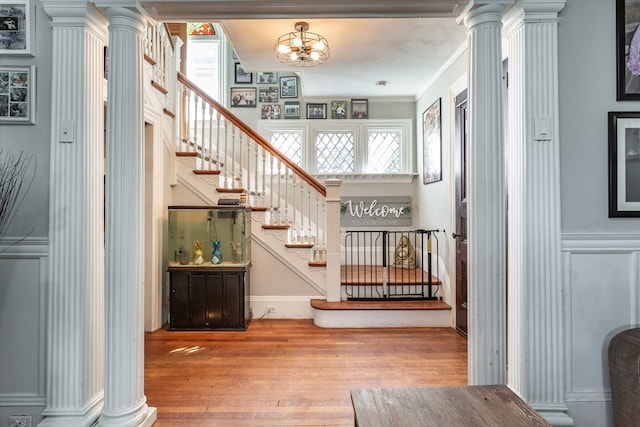 entryway featuring ornamental molding, a notable chandelier, wood-type flooring, and decorative columns