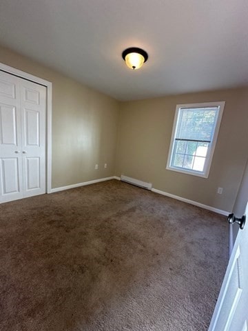 unfurnished bedroom featuring a baseboard radiator, dark carpet, and a closet