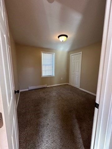 unfurnished bedroom with baseboard heating and dark carpet