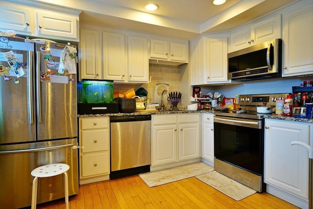 kitchen featuring appliances with stainless steel finishes, dark stone counters, white cabinets, and light wood finished floors