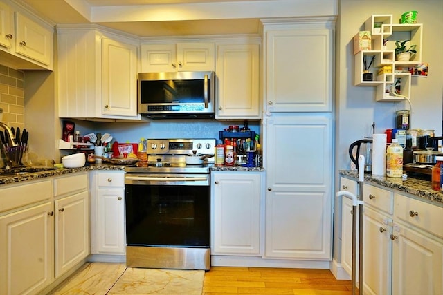 kitchen featuring white cabinets, dark stone counters, appliances with stainless steel finishes, light wood-style floors, and a sink