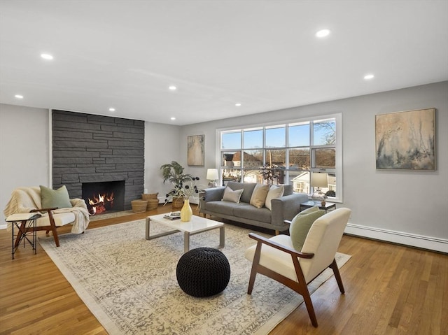 living room with a baseboard heating unit, a fireplace, and light hardwood / wood-style flooring