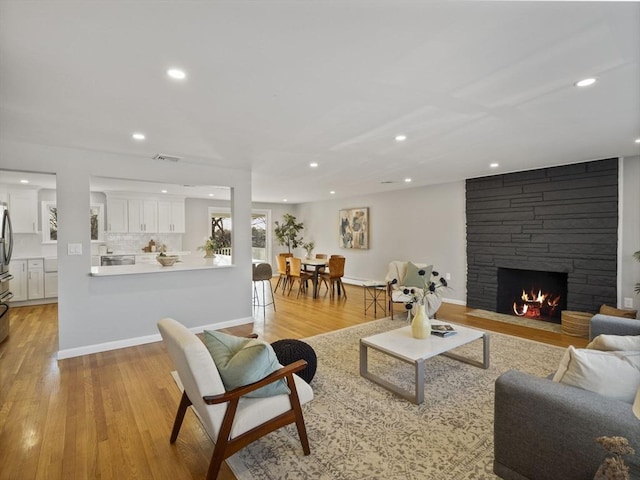 living room with a stone fireplace and light wood-type flooring