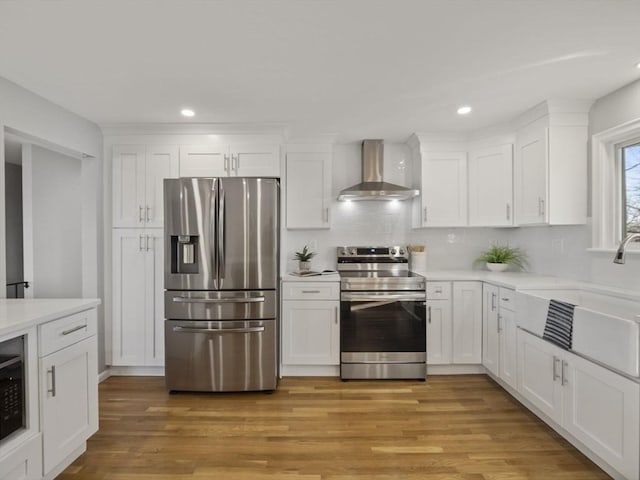 kitchen with wall chimney exhaust hood, sink, light wood-type flooring, appliances with stainless steel finishes, and white cabinets