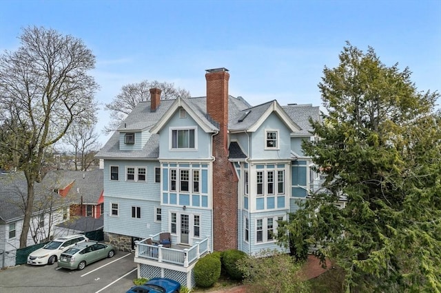 rear view of property featuring uncovered parking, a shingled roof, and a chimney