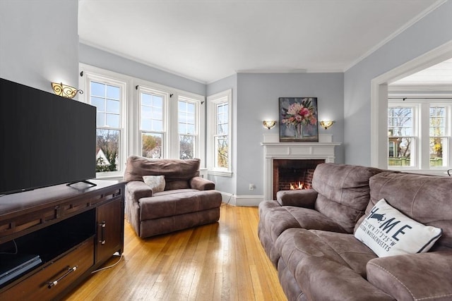 living area featuring light wood-type flooring, crown molding, baseboards, and a brick fireplace