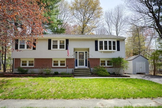split foyer home with a storage unit, brick siding, a front yard, entry steps, and an outbuilding