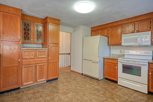 kitchen with white appliances, a textured ceiling, brown cabinetry, and glass insert cabinets