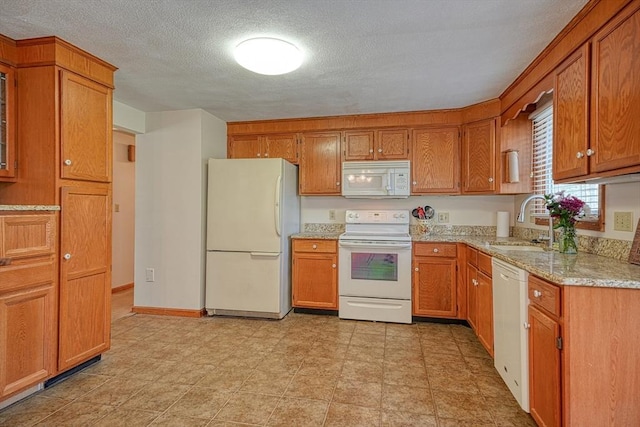 kitchen featuring a sink, brown cabinets, light stone countertops, and white appliances