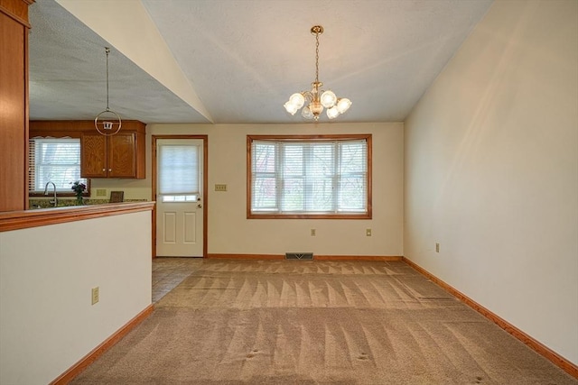 unfurnished dining area featuring light colored carpet, visible vents, a sink, baseboards, and a chandelier