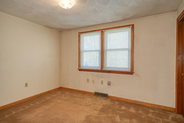 carpeted spare room featuring a textured ceiling, baseboards, and visible vents