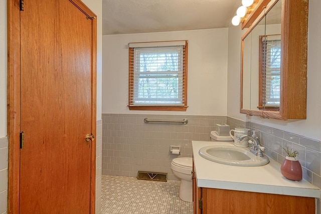 bathroom with vanity, wainscoting, toilet, tile walls, and tile patterned floors