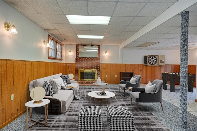 living room with a drop ceiling, a brick fireplace, a wainscoted wall, and wooden walls
