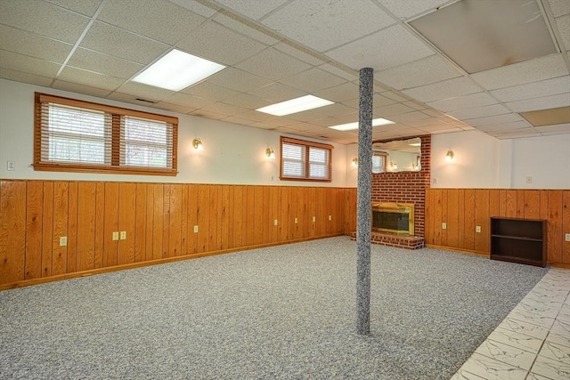 below grade area with marble finish floor, wainscoting, a brick fireplace, wooden walls, and a paneled ceiling