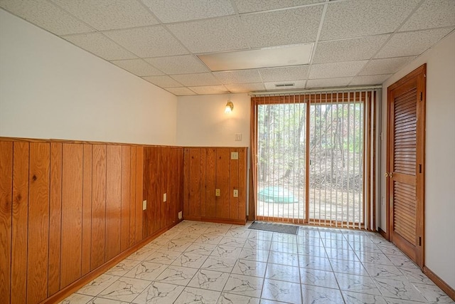 unfurnished room with wood walls, a paneled ceiling, marble finish floor, a wainscoted wall, and visible vents