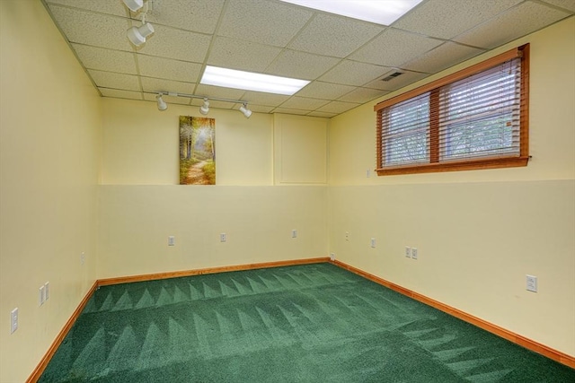 basement with carpet flooring, rail lighting, a paneled ceiling, and baseboards