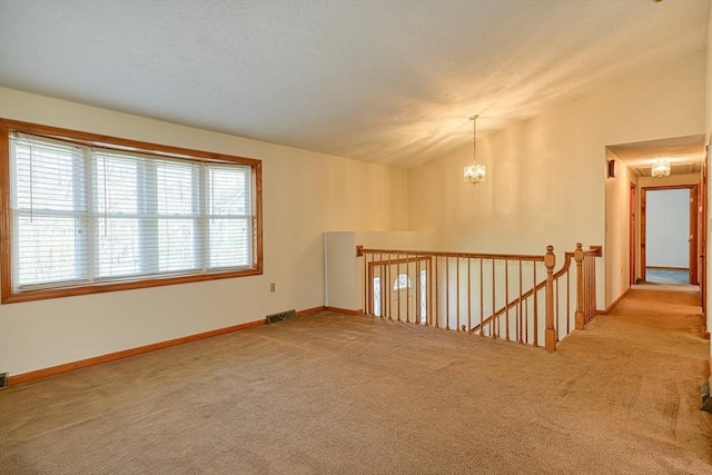 spare room featuring a notable chandelier, carpet, baseboards, lofted ceiling, and visible vents