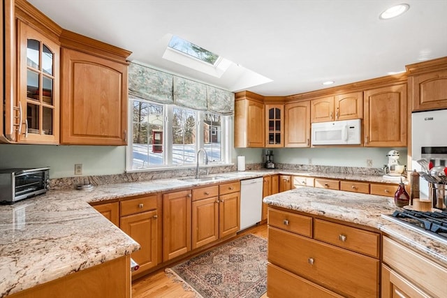 kitchen featuring light stone counters, a toaster, white appliances, a skylight, and a sink