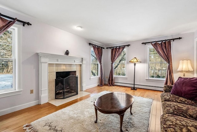 living area featuring a baseboard heating unit, wood-type flooring, a fireplace, and baseboards