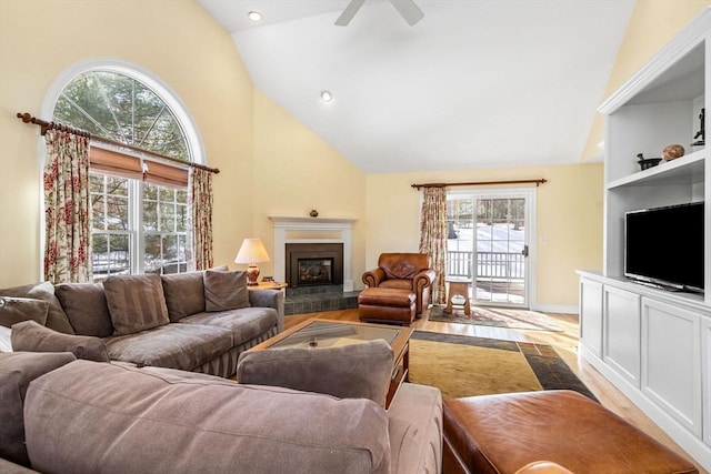 living room featuring high vaulted ceiling, a glass covered fireplace, wood finished floors, and a ceiling fan