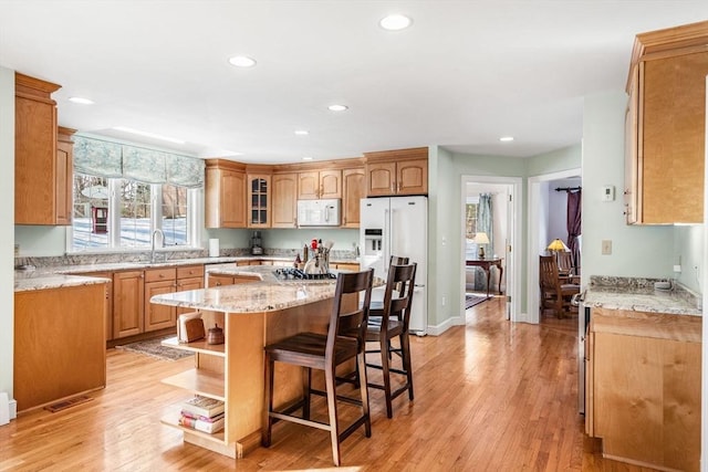 kitchen with a breakfast bar, a center island, open shelves, light wood-style floors, and white appliances