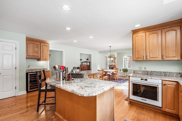 kitchen featuring beverage cooler, a center island, oven, light wood-type flooring, and a kitchen bar