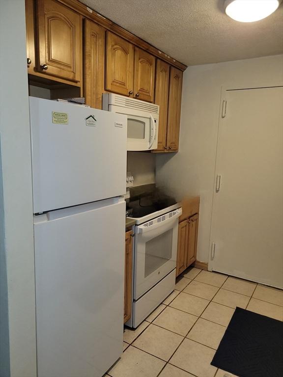 4 Post Oak Ln Unit 15, Natick, MA 01760 - kitchen with white appliances, light tile patterned floors, brown cabinetry, and a textured ceiling
