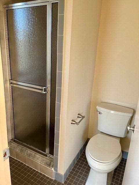 bathroom with toilet, a shower with door, and tile patterned flooring