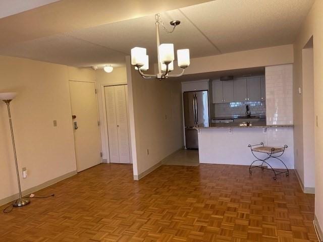 kitchen featuring a chandelier, stainless steel refrigerator, kitchen peninsula, pendant lighting, and backsplash