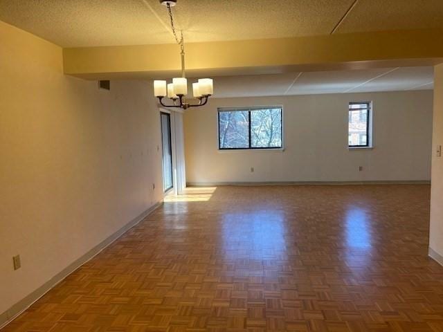 unfurnished room featuring a textured ceiling, a chandelier, and parquet flooring