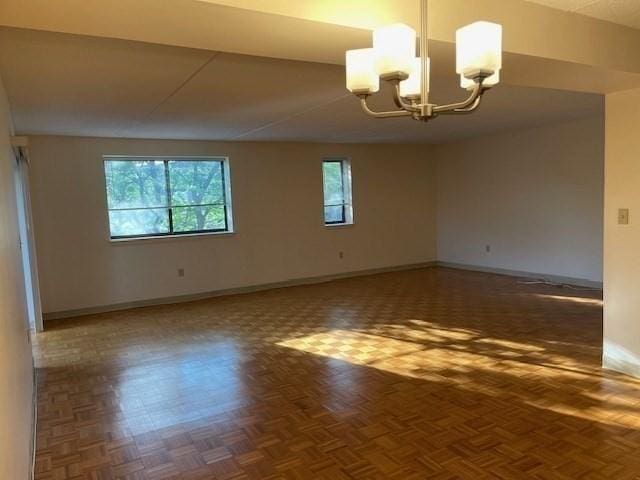 empty room featuring dark parquet floors and an inviting chandelier