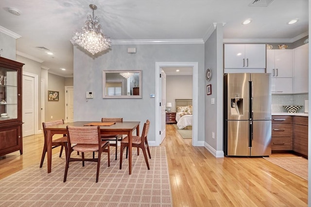 dining room featuring light wood-style floors, baseboards, crown molding, and a notable chandelier