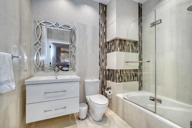 full bathroom with vanity, tiled shower / bath, toilet, and tile walls