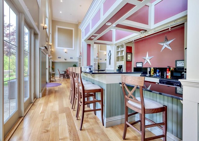 kitchen with a kitchen breakfast bar, dark countertops, a wainscoted wall, and light wood-type flooring