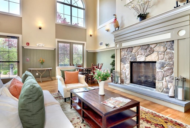 living room featuring a stone fireplace, a high ceiling, wood finished floors, and visible vents