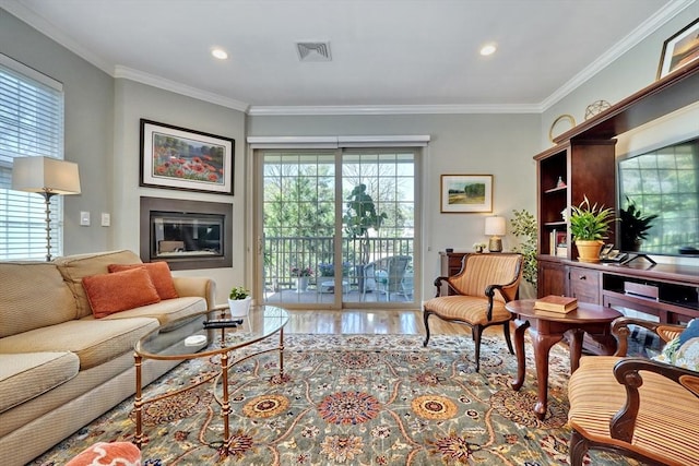 living area with crown molding, a glass covered fireplace, wood finished floors, and visible vents