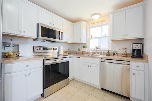 kitchen featuring appliances with stainless steel finishes, a sink, white cabinetry, and light tile patterned floors