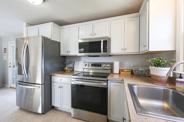 kitchen with appliances with stainless steel finishes, a sink, light countertops, white cabinetry, and light tile patterned floors