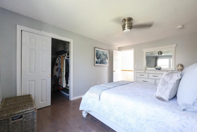 bedroom with dark wood-style floors, a spacious closet, a closet, baseboards, and a ceiling fan
