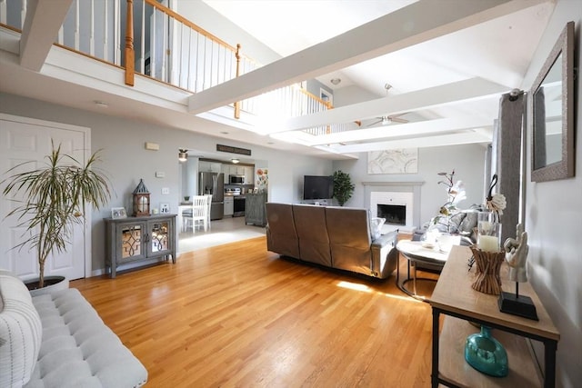 living area featuring ceiling fan, a fireplace, light wood-type flooring, high vaulted ceiling, and beamed ceiling