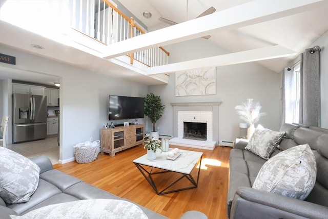 living area with a baseboard radiator, light wood-style floors, a brick fireplace, and baseboards
