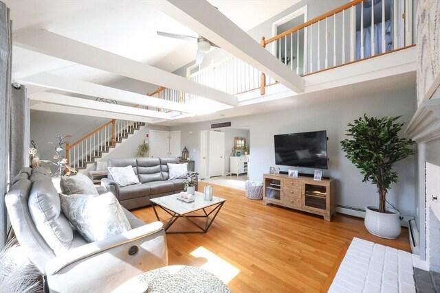 living room featuring baseboard heating, stairway, a towering ceiling, wood finished floors, and ceiling fan