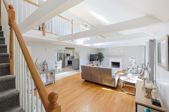 living area featuring stairs, wood finished floors, high vaulted ceiling, a fireplace with raised hearth, and beamed ceiling